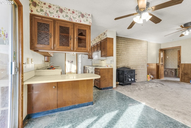 kitchen with sink, white appliances, ceiling fan, dark colored carpet, and a wood stove