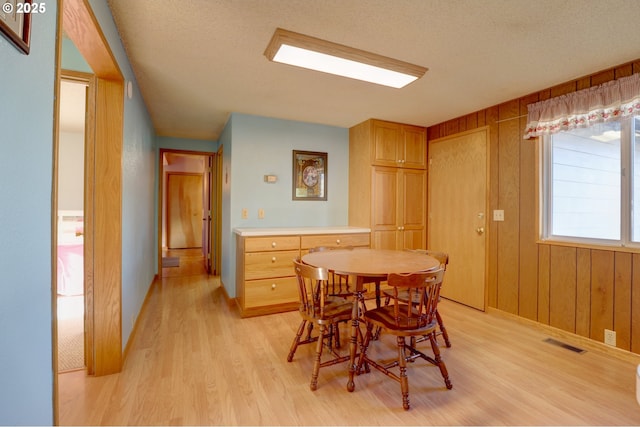 dining area with light wood-type flooring, visible vents, wooden walls, and a textured ceiling