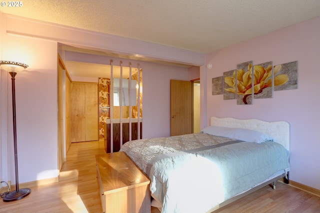 bedroom featuring baseboards, a textured ceiling, and light wood finished floors