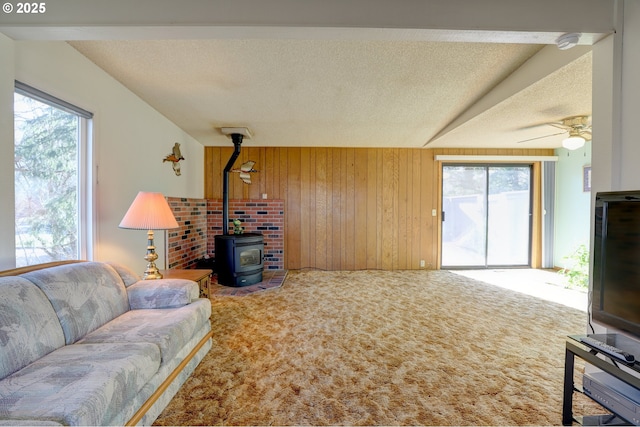 living area featuring a ceiling fan, a wood stove, carpet flooring, wood walls, and a textured ceiling