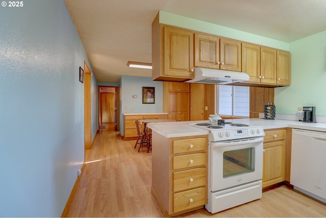 kitchen featuring white appliances, light countertops, under cabinet range hood, and a peninsula