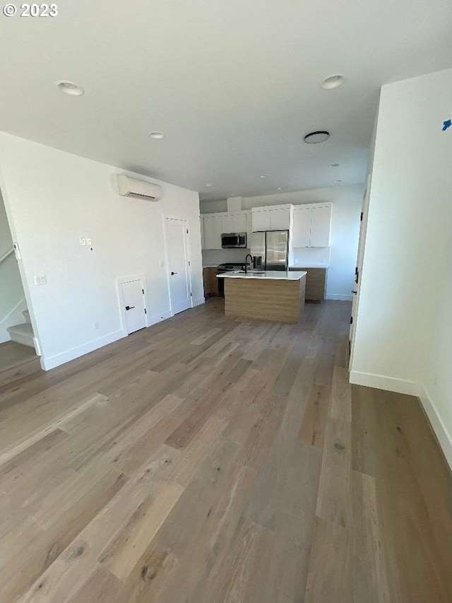 kitchen featuring white cabinetry, a center island with sink, light wood-type flooring, an AC wall unit, and appliances with stainless steel finishes