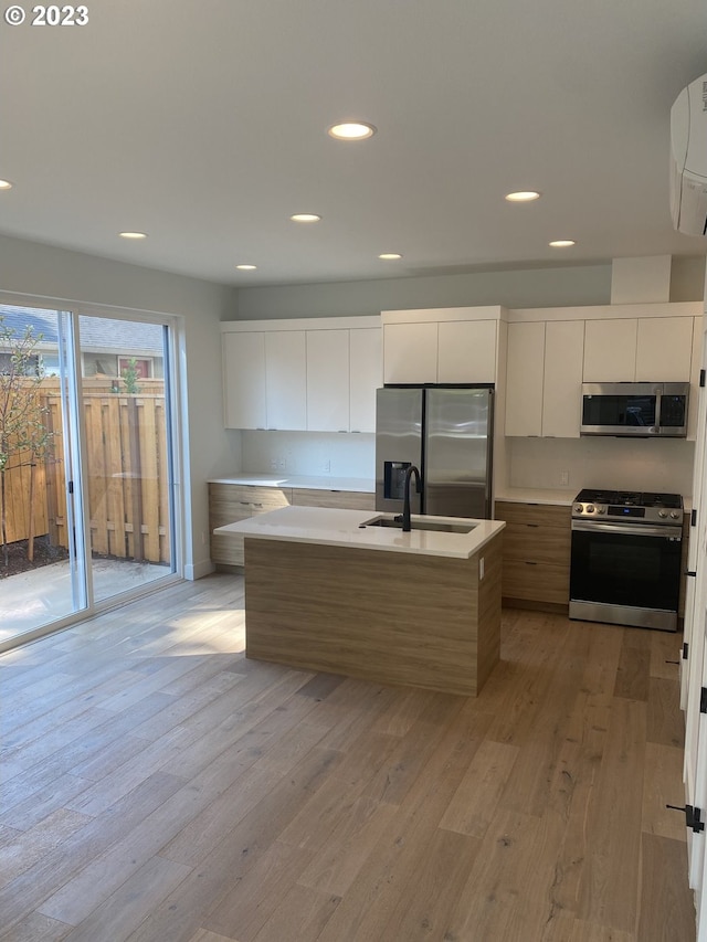 kitchen with light hardwood / wood-style flooring, stainless steel appliances, white cabinets, and a center island with sink