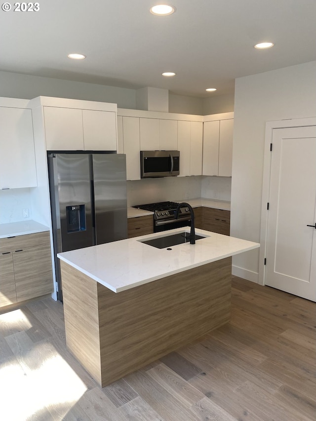 kitchen featuring an island with sink, white cabinetry, sink, stainless steel appliances, and light hardwood / wood-style flooring