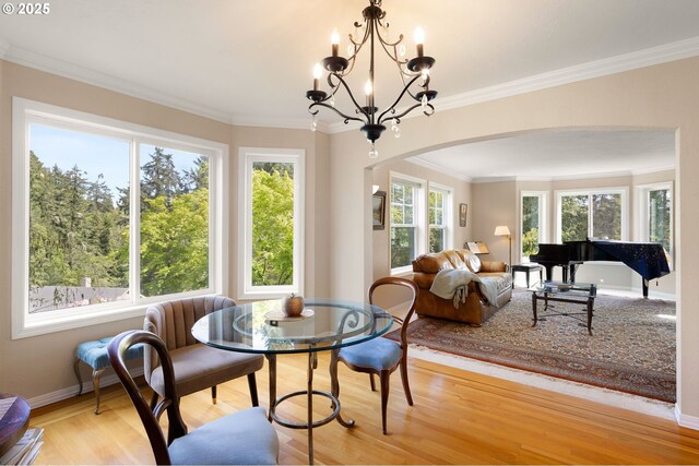 dining room featuring crown molding, arched walkways, a notable chandelier, and light wood-style flooring
