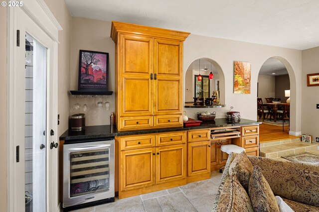 kitchen featuring dark countertops, arched walkways, brown cabinets, and beverage cooler
