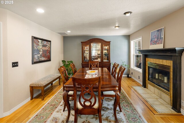 dining area featuring recessed lighting, baseboards, a tiled fireplace, and light wood-style floors
