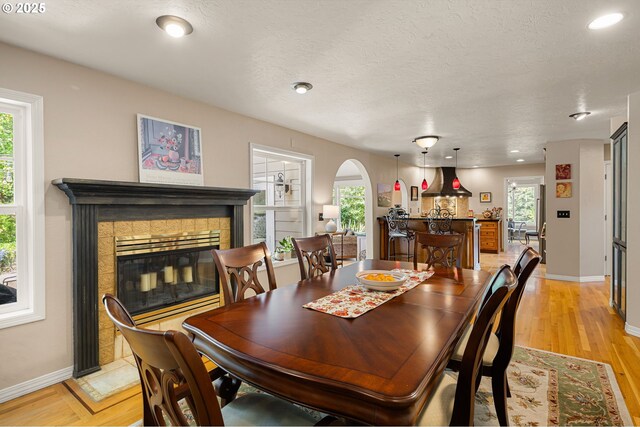 dining area featuring a fireplace, baseboards, recessed lighting, light wood-type flooring, and arched walkways