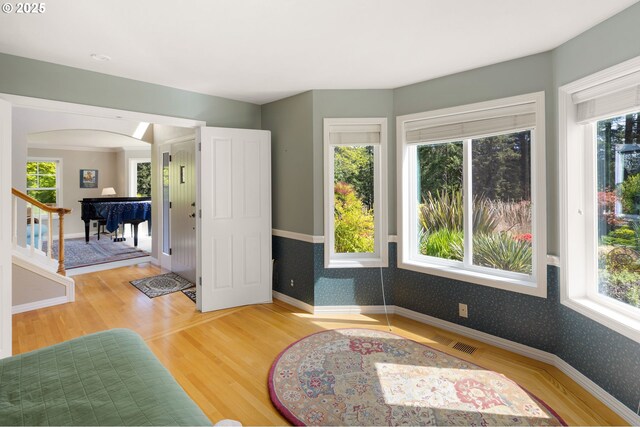 interior space featuring arched walkways, baseboards, wallpapered walls, wood finished floors, and visible vents