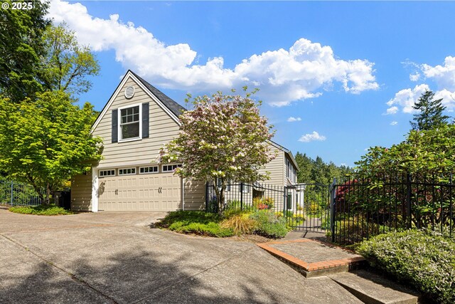 view of property hidden behind natural elements featuring fence, a gate, an attached garage, and driveway