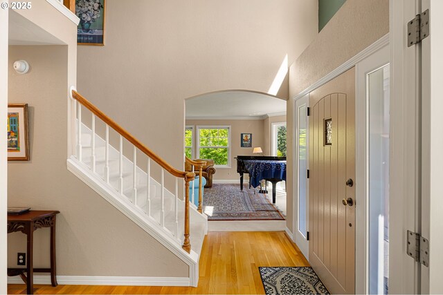 foyer entrance with wood finished floors, baseboards, a high ceiling, stairway, and arched walkways