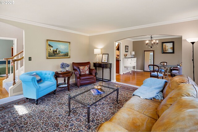 living room with crown molding, an inviting chandelier, arched walkways, stairs, and wood finished floors