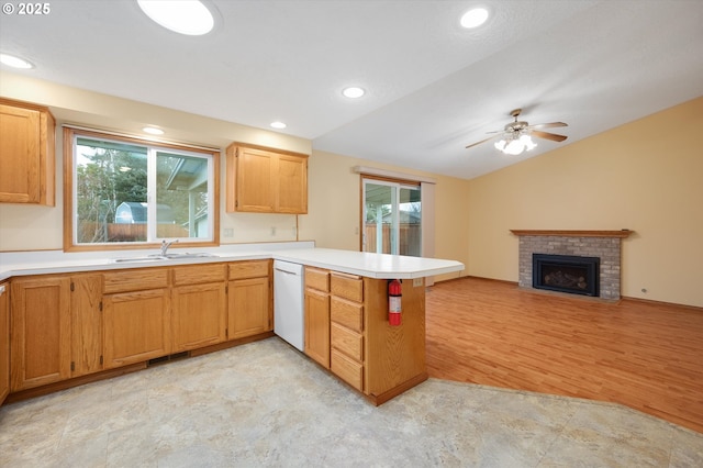 kitchen featuring lofted ceiling, sink, white dishwasher, a brick fireplace, and kitchen peninsula