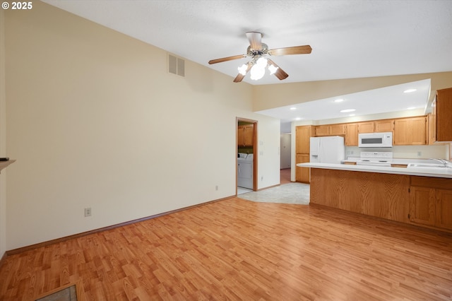 kitchen featuring vaulted ceiling, washer / dryer, kitchen peninsula, white appliances, and light hardwood / wood-style flooring