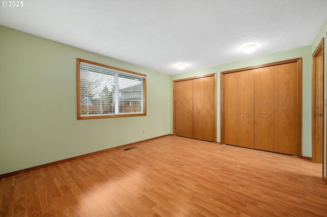 unfurnished bedroom with two closets, light hardwood / wood-style floors, and a textured ceiling