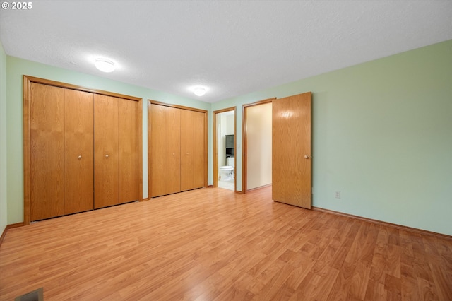 unfurnished bedroom with two closets, ensuite bath, a textured ceiling, and light wood-type flooring