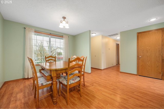 dining area with an inviting chandelier, a textured ceiling, and light hardwood / wood-style floors