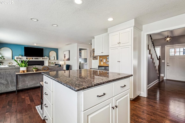 kitchen with dark wood-style floors, a center island, white cabinetry, and dark stone countertops