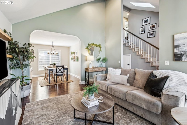 living room with a notable chandelier, wood finished floors, high vaulted ceiling, baseboards, and stairs