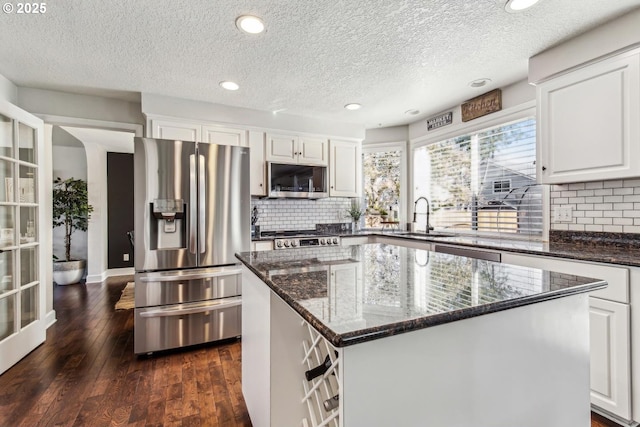 kitchen with stainless steel appliances, a sink, white cabinets, dark wood-style floors, and dark stone countertops