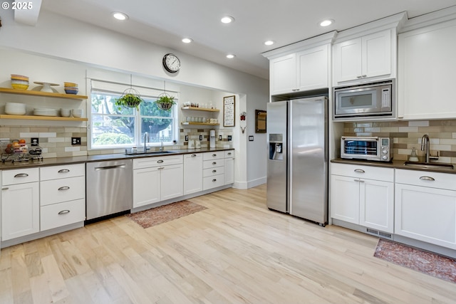 kitchen with open shelves, appliances with stainless steel finishes, dark countertops, a sink, and a toaster
