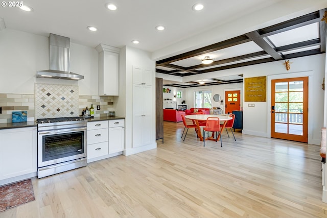 kitchen with wall chimney range hood, dark countertops, decorative backsplash, and stainless steel gas stove