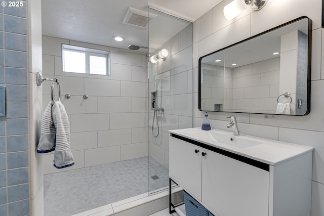 full bathroom featuring vanity, tile walls, tiled shower, and visible vents
