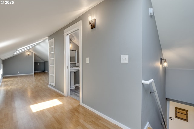 interior space with wood finished floors, lofted ceiling, baseboards, built in shelves, and an upstairs landing