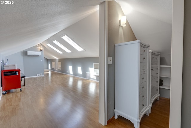 additional living space featuring a wall unit AC, lofted ceiling with skylight, wood finished floors, and visible vents