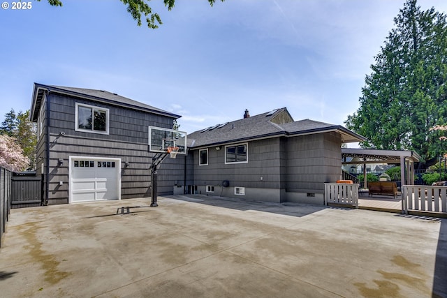 back of property with driveway, roof with shingles, a deck, fence, and an attached garage