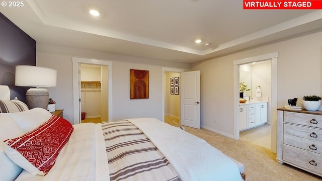 carpeted bedroom featuring a closet, a raised ceiling, a walk in closet, and ensuite bath