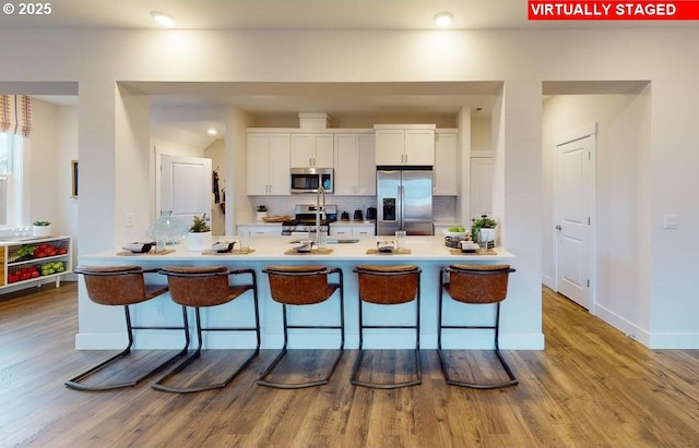 kitchen with white cabinets, backsplash, a kitchen bar, and stainless steel appliances