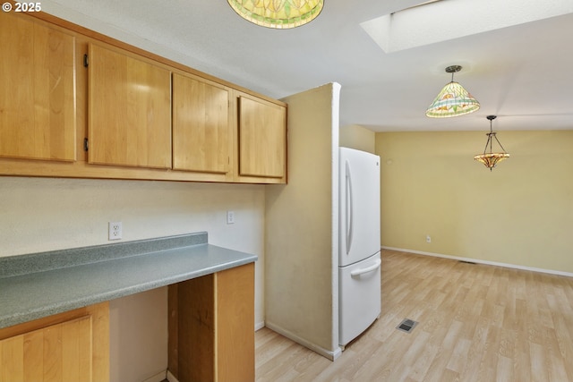 kitchen featuring freestanding refrigerator, a skylight, light wood finished floors, and baseboards
