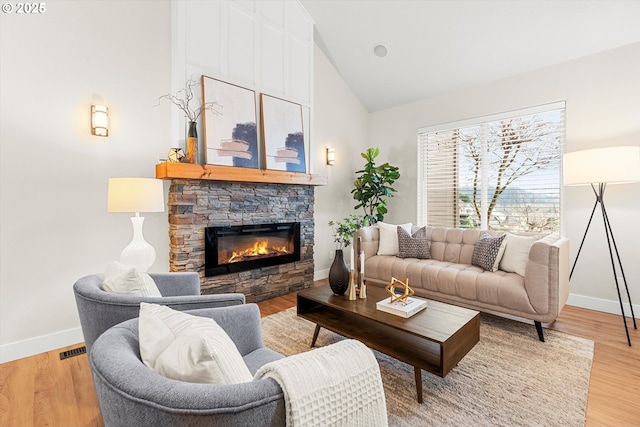 living room with a stone fireplace, high vaulted ceiling, and light wood-type flooring