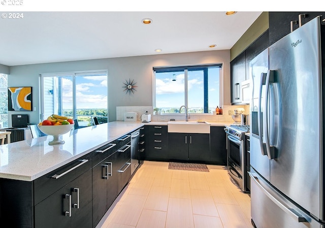 12508 NW Mountain View Rd, Portland, OR 97231 - kitchen featuring dark cabinetry, a peninsula, appliances with stainless steel finishes, and a healthy amount of sunlight
