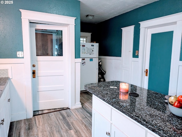 kitchen with white cabinetry, a textured ceiling, light wood-type flooring, white fridge, and dark stone counters