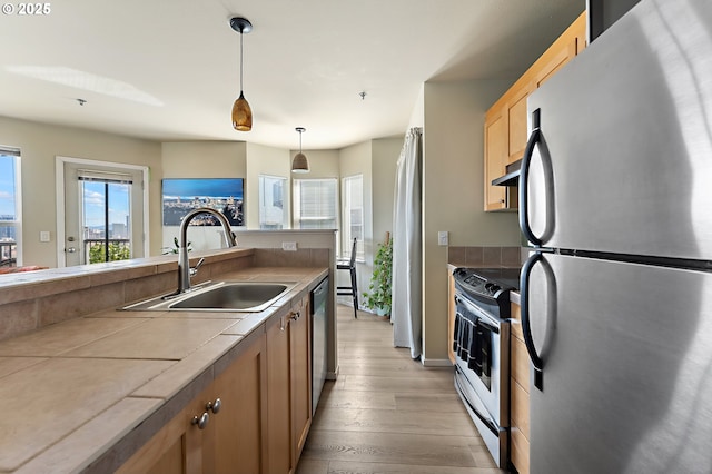 410 NW Uptown Ter Unit 3-B, Portland, OR 97210 - kitchen featuring stainless steel appliances, a sink, light wood finished floors, decorative light fixtures, and under cabinet range hood