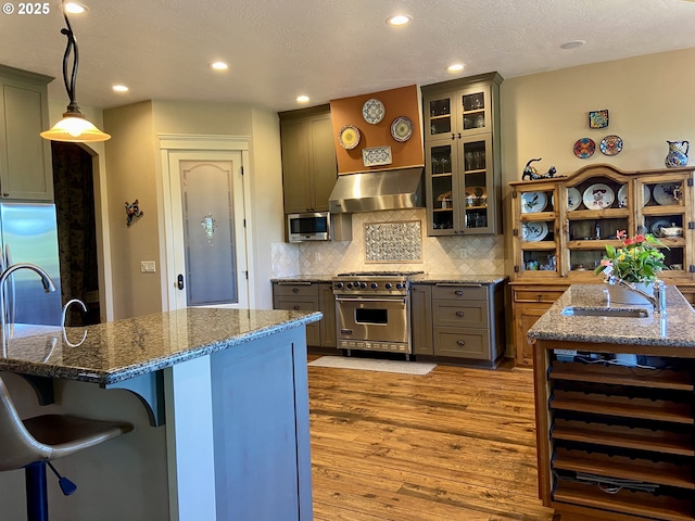 625 St Andrews Loop, Creswell, OR 97426 - kitchen featuring appliances with stainless steel finishes, exhaust hood, a sink, dark stone countertops, and light wood finished floors