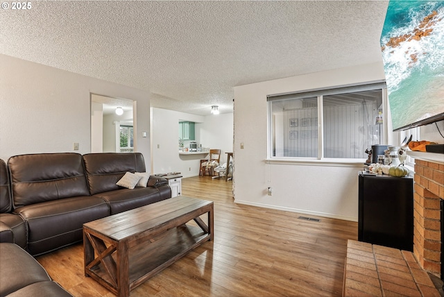 living room with a brick fireplace, a textured ceiling, and light hardwood / wood-style floors