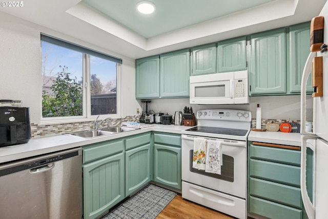 kitchen featuring a tray ceiling, green cabinets, white appliances, and light hardwood / wood-style flooring