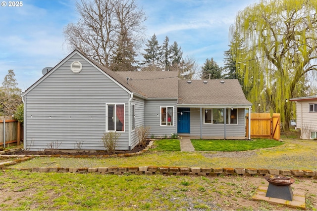 back of property featuring a lawn, an outdoor fire pit, roof with shingles, and fence