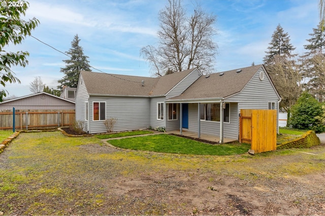 rear view of house with a patio, a lawn, roof with shingles, and fence