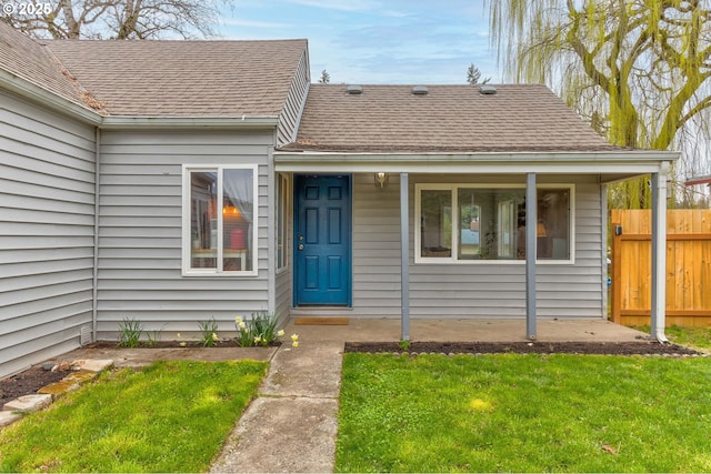 entrance to property with a shingled roof, a yard, and fence