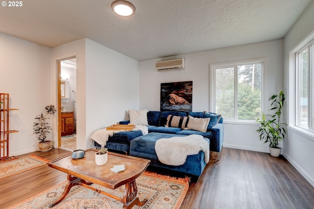 living room with a wall mounted air conditioner, baseboards, a textured ceiling, and wood finished floors