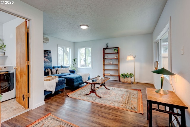 living area with a wall mounted air conditioner, wood finished floors, heating unit, a textured ceiling, and washer / clothes dryer