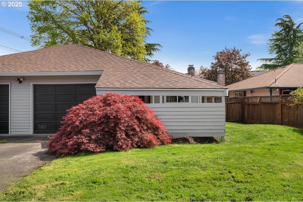 view of home's exterior with fence, a shingled roof, a lawn, and a garage
