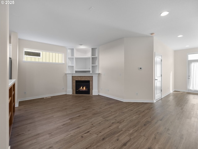 unfurnished living room featuring built in features, plenty of natural light, dark hardwood / wood-style flooring, and a tile fireplace