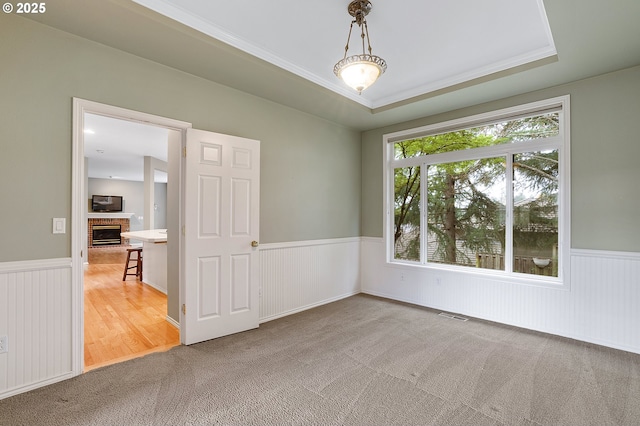 unfurnished room with a tray ceiling, wainscoting, a brick fireplace, and carpet floors