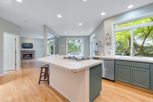 kitchen featuring tile countertops, white gas cooktop, light wood finished floors, dishwasher, and a sink