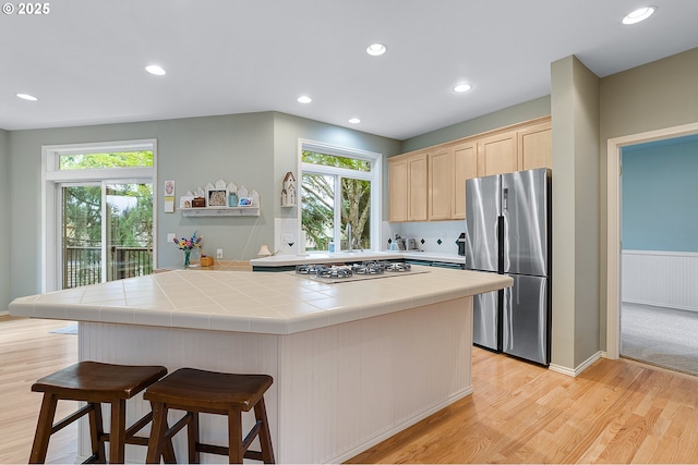 kitchen with tile countertops, freestanding refrigerator, a wealth of natural light, light brown cabinets, and white gas cooktop